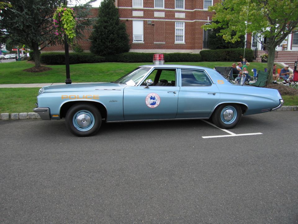 Light blue police sedan with round door seal, side profile view