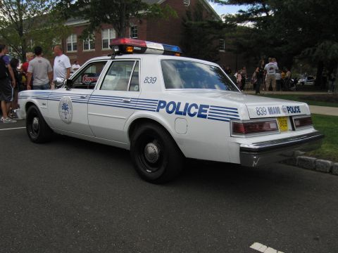 1991 Ford LTD Crown Victoria - white Miami Police sedan numbered 839 with blue striping, POLICE lettering and a roof light bar at the curb.