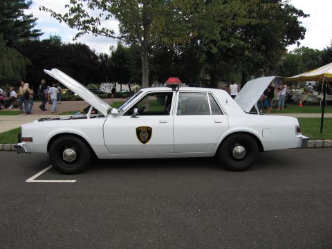 1991 Ford LTD Crown Victoria - Side profile of a white police sedan with both hood and trunk open and a round door shield, parked at a curb.