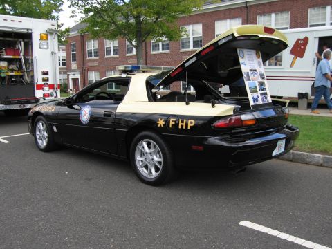 1991 Ford LTD Crown Victoria - black-and-tan Chevrolet Camaro marked 'FHP' and 'STATE TROOPER' with its hatch open showing a display board.