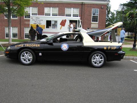 1991 Ford LTD Crown Victoria - black-and-tan Chevrolet Camaro lettered 'STATE TROOPER' and 'FHP' parked in profile near an ice cream truck.