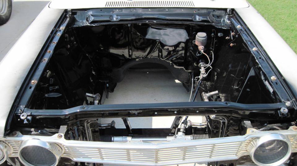 Empty engine bay with black inner fenders and firewall, showing brake master cylinder and steering components