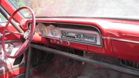 1992 Ford Mustang - The interior of a classic red car shows a vintage radio and gauges, along with a prominent roll cage.