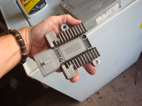 1989 Ford Bronco - A hand holds a Ford voltage regulator, with a Ford-branded electronic control unit visible in the background.