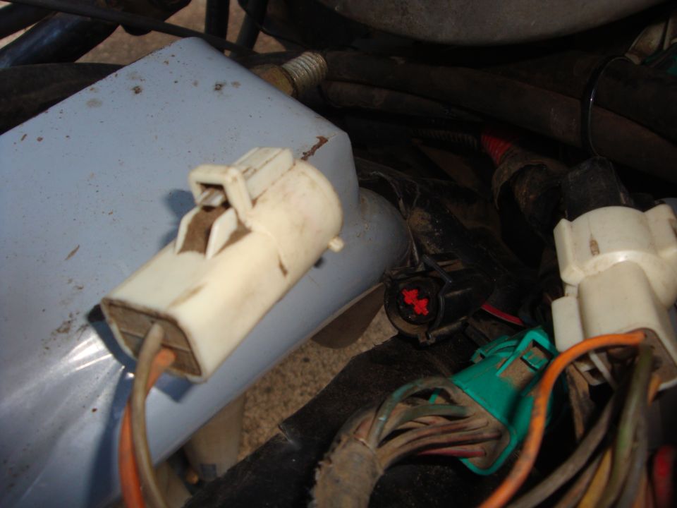 Close-up of white and green unplugged wiring harness connectors on a blue washer reservoir