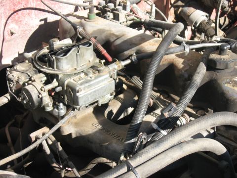 1981 Ford Bronco - A Holley four-barrel carburetor sits uncovered on a cast aluminum intake manifold in a V8 engine bay, with throttle linkage, a red plug wir…
