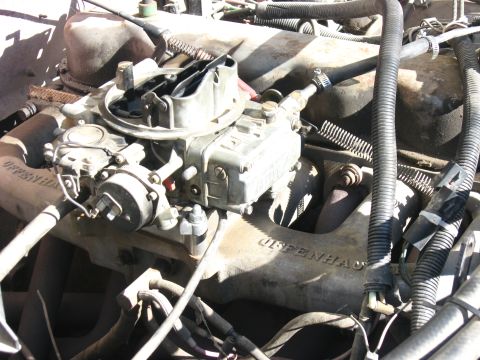1981 Ford Bronco - A Holley-style four-barrel carburetor with the air cleaner removed, mounted on a cast aluminum intake manifold in a dusty V8 engine bay. Va…