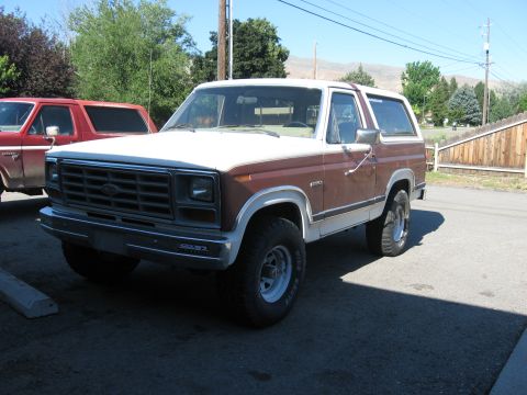 1981 Ford Bronco - A two-tone Ford Bronco is parked on asphalt next to a red Ford truck.