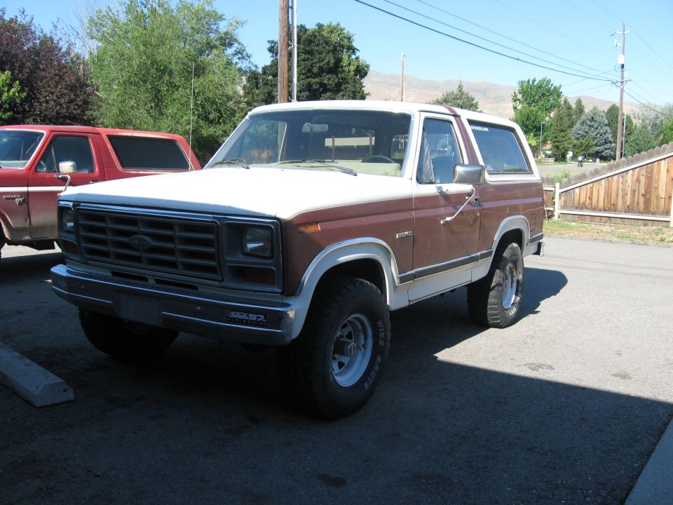 Brown and white Ford Bronco parked next to a red Ford truck