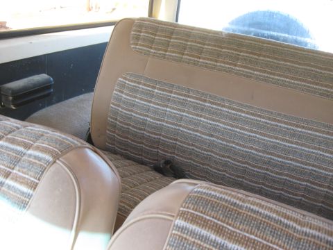 1981 Ford Bronco - The interior of a Ford Bronco shows striped upholstery on the rear seats and a spare tire visible through the window.