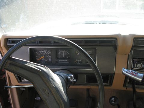 1981 Ford Bronco - Interior view from the driver's seat of a tan-dash truck showing the black two-spoke steering wheel, 85 mph speedometer marked 'Unleaded Fu…