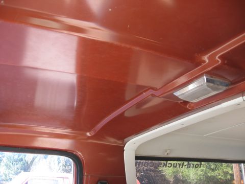 1981 Ford Bronco - Interior view looking up at a bare painted metal headliner in reddish-orange, with the exposed roof bows and a chrome-bezel rectangular dom…