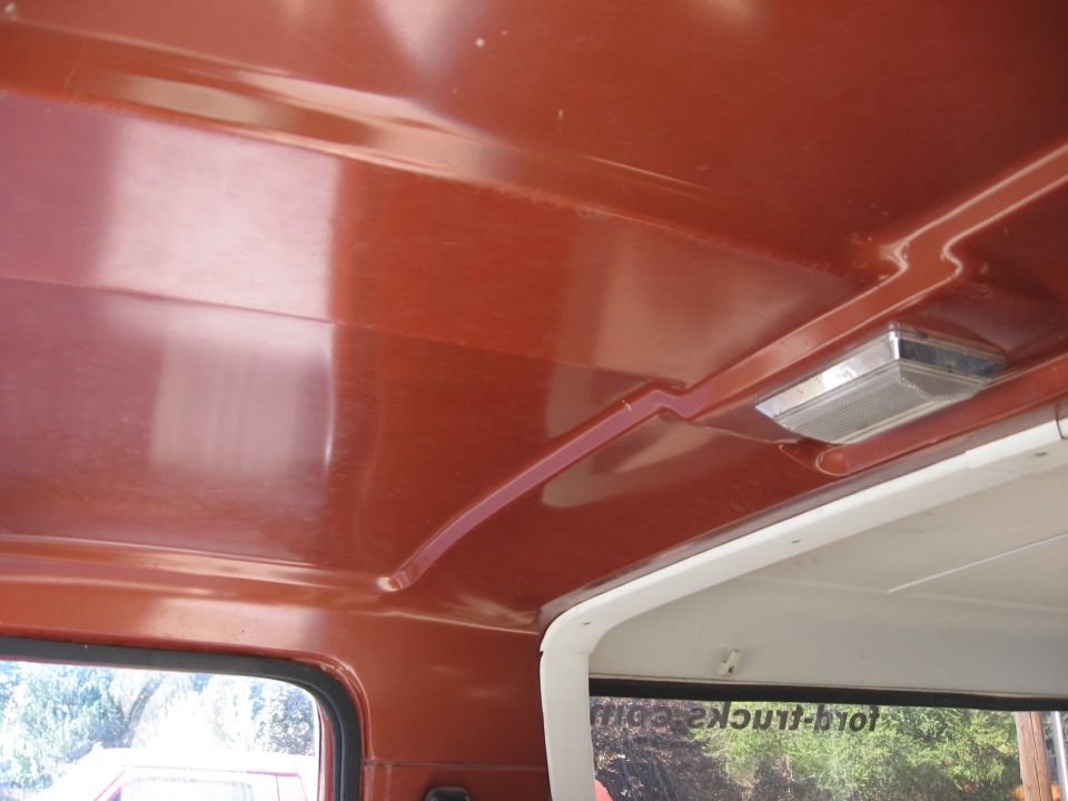 Bare reddish-orange painted metal headliner with chrome dome light inside a truck cab
