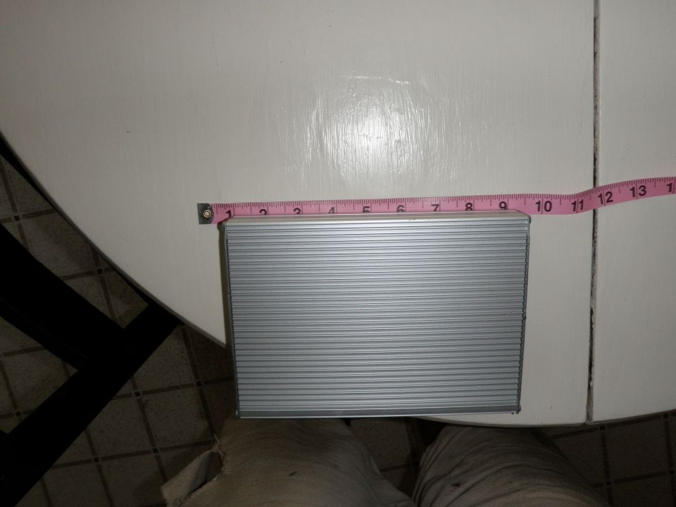 Silver rectangular object with horizontal ridges, being measured with a pink tape measure