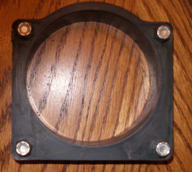 Black rubber gasket with four bolt holes, placed on a wooden surface
