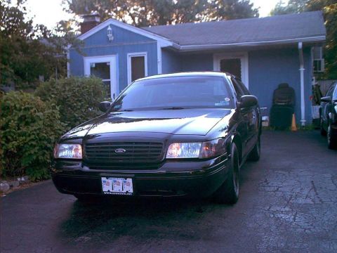 2000 Ford Crown Victoria - A black 2000 Ford Crown Victoria is parked in front of a blue house. The vehicle has a custom license plate.