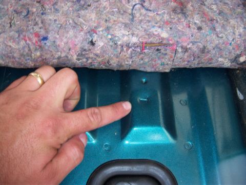 1996 Ford Bronco - A hand points to a small metal tab on the teal interior of a vehicle, with carpet overhead.