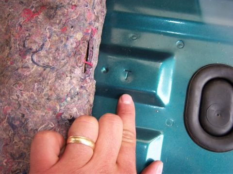 1996 Ford Bronco - A finger points to a stamped letter T on a teal interior panel, next to a rubber grommet.