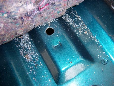 1996 Ford Bronco - Close-up of a teal interior floor showing metal shavings and a drilled hole, possibly related to child seat tether installation.
