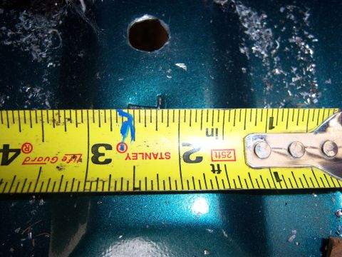 1996 Ford Bronco - A yellow tape measure is used to measure the diameter of a hole on a teal-colored surface.
