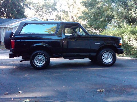 1996 Ford Bronco - A black Ford Bronco is parked on a driveway with trees and a house in the background.