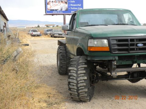1989 Ford Bronco - Green Ford F-Series truck with oversized tires and aftermarket bumper. Other vehicles visible in background.