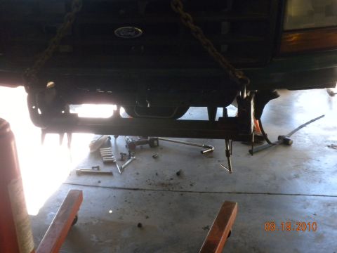 1989 Ford Bronco - The front end of a 1989 Ford Bronco is suspended by chains, with tools scattered on the garage floor below.