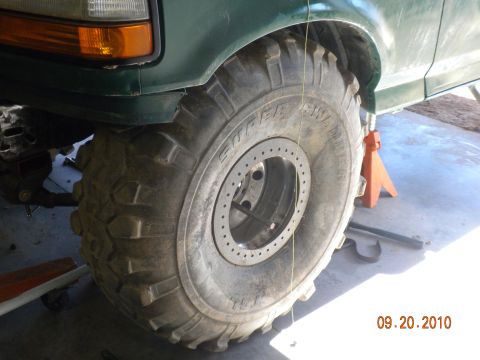 1989 Ford Bronco - A green SUV's front tire and fender are visible, supported by an orange jack stand.