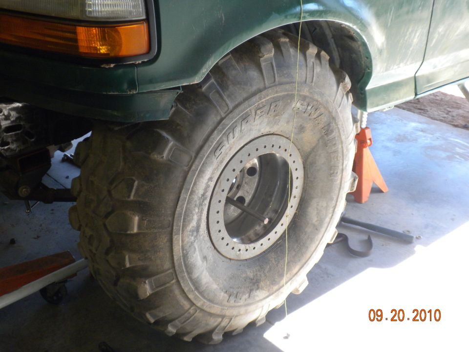 Green SUV's front tire and fender, lifted on an orange jack stand. Large off-road tire with beadlock wheel