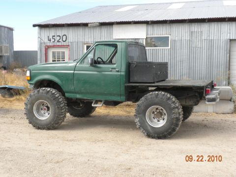 1989 Ford Bronco - This modified truck, likely from the early to mid-1990s, features a flatbed and massive off-road tires.