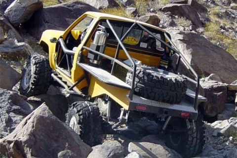 1989 Ford Bronco - Yellow off-road vehicle navigates rocky terrain with a custom roll cage and spare tire.