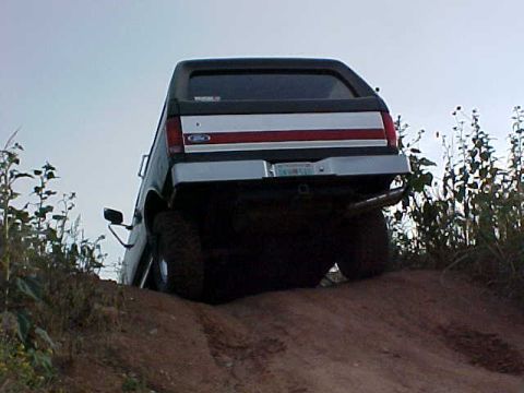 1989 Ford Bronco - Rear view of a 1989 Ford Bronco climbing a dirt hill with vegetation on the sides.