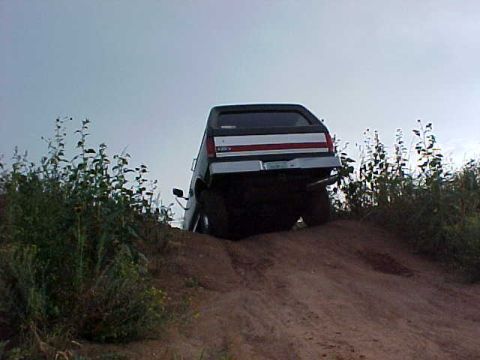 1989 Ford Bronco - This SUV is shown from the rear as it ascends a sandy incline, with vegetation flanking the path.