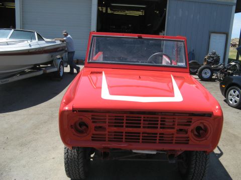 1966 Ford Bronco - A red 1966 Ford Bronco is parked in front of a garage, with a boat on a trailer to its left.