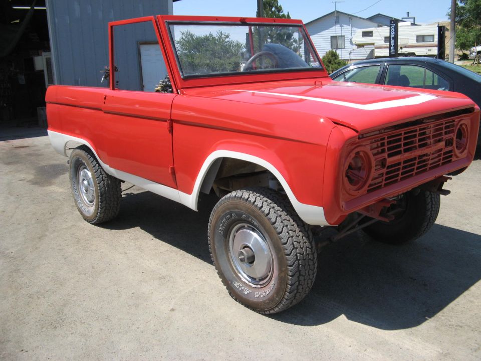 Red 1966 Ford Bronco with white trim and a white stripe on the hood, parked outdoors