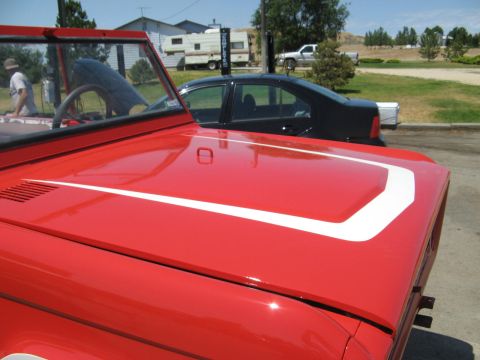 1966 Ford Bronco - A red SUV with a white stripe on its hood is parked outdoors.
