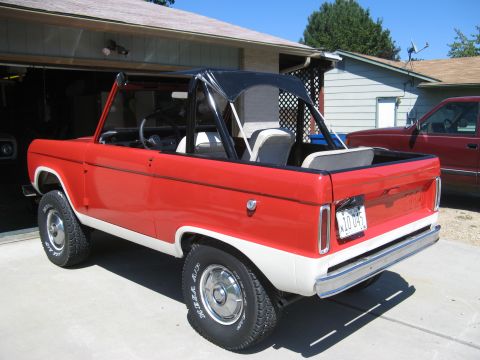 1966 Ford Bronco - Red and white 1966 Ford Bronco with a black soft top is parked outside a garage.