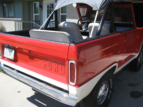 1966 Ford Bronco - Rear view of a red and white Ford Bronco with a chrome bumper and "FORD" embossed on the tailgate.