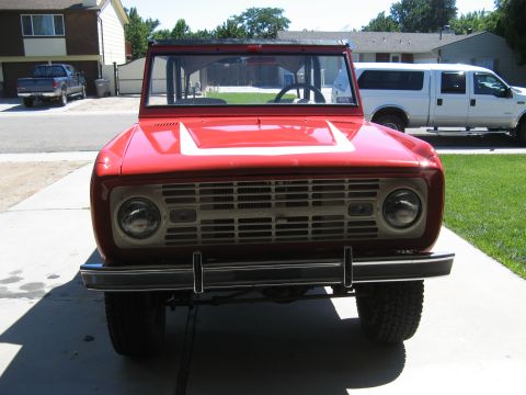 1966 Ford Bronco - This red 1966 Ford Bronco is parked in a driveway with other vehicles visible in the background.