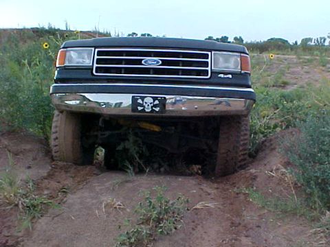 1989 Ford Bronco - A dark green 1987 Ford Bronco is stuck in the dirt, its front end angled towards the camera.