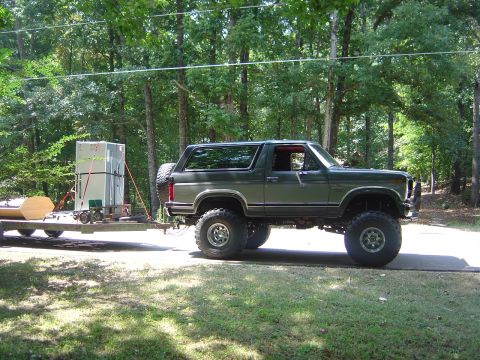 1986 Ford Bronco - A lifted 1986 Ford Bronco is shown from the side, towing a trailer loaded with appliances and other cargo.