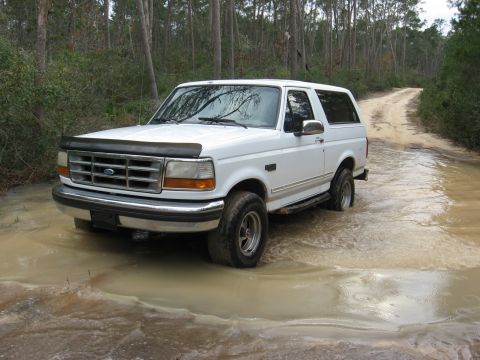 1994 Ford Bronco - This 1994 Ford Bronco navigates a water-filled dirt road surrounded by trees.