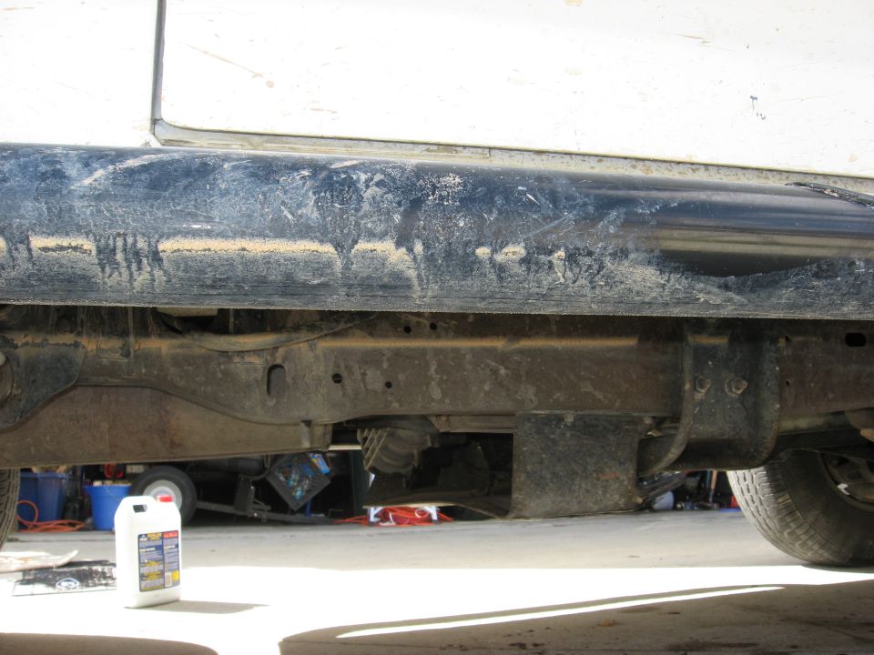 side view of dirty vehicle frame, showing suspension and a bottle of fluid on the ground