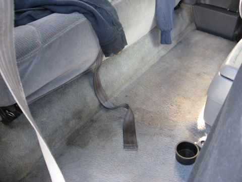 1994 Ford Bronco - The interior of a vehicle shows the rear seating area and carpeted floor with a seatbelt and a cup holder visible.