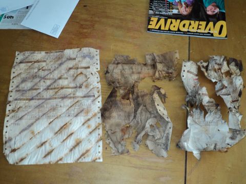 1974 Ford Elite - Several damaged paper documents and a magazine are spread out on a wooden table.