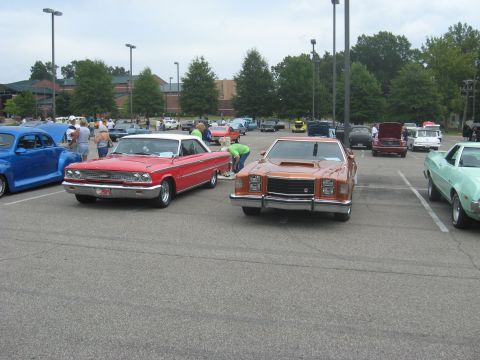 1972 Ford Ranchero - This orange coupe with a prominent hood scoop is parked in a lot with other vehicles.