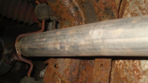 1988 Ford Bronco - Close-up view of a vehicle's exhaust pipe and rusty undercarriage components.