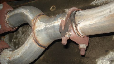 1988 Ford Bronco - Close-up view of a vehicle's exhaust pipe connection, showing a rusty clamp and bolts. The registry claims this is from a 1988 Ford Bronco,…