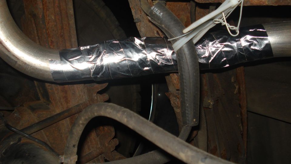 Exhaust pipe wrapped in silver tape with a black hose secured by zip ties