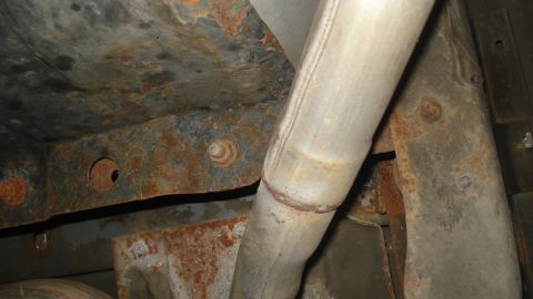 1988 Ford Bronco - The undercarriage of a vehicle displays significant rust on its frame and exhaust system components.